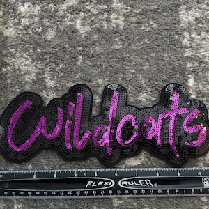 May include: A black and purple sequined patch with the word "Wildcats" in a stylized font.