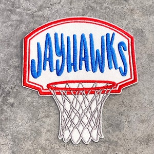 May include: A white embroidered patch with a red border, depicting a basketball hoop with the word "JAYHAWKS" in blue lettering.