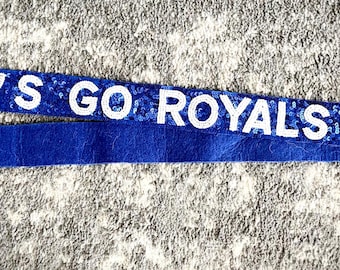 May include: Blue and gold fabric strap with the text "LET'S GO ROYALS" and a gold crown.