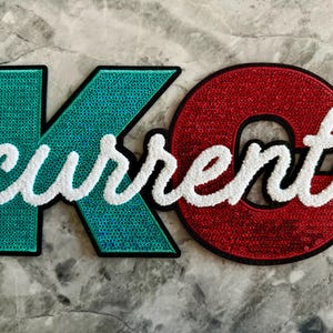 May include: A green and red felt patch with the word "current" in white fluffy letters.