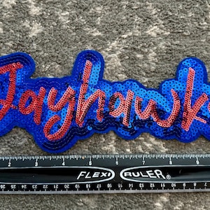 May include: Blue and red sequined patch with the word "Jayhawks" in a stylized font.