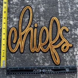 May include: A gold sequined patch with the word "chiefs" in black outlined lettering.