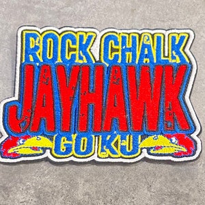 May include: A red, blue, and yellow embroidered patch with the words "Rock Chalk Jayhawk Go KU" and a stylized image of a Jayhawk bird.