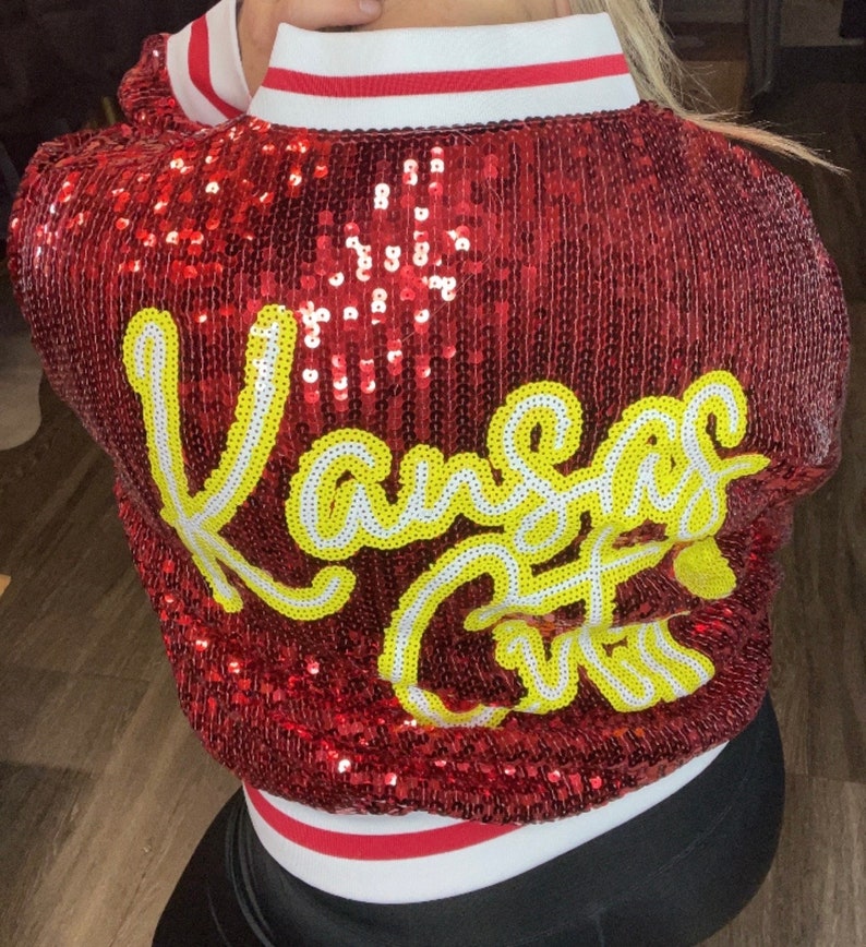 K&ouml;nnte beinhalten: Rote Paillettenjacke mit dem Schriftzug "Kansas City" in gelber und wei&szlig;er Schrift auf dem R&uuml;cken. Die Jacke hat einen wei&szlig;en Kragen mit roten und wei&szlig;en Streifen.