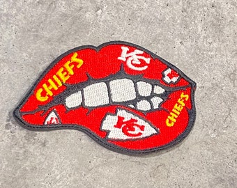 May include: Embroidered patch featuring a red mouth design with white teeth and the word "CHIEFS" in yellow. The patch also includes the team's logo in white and red. The patch has a black border.