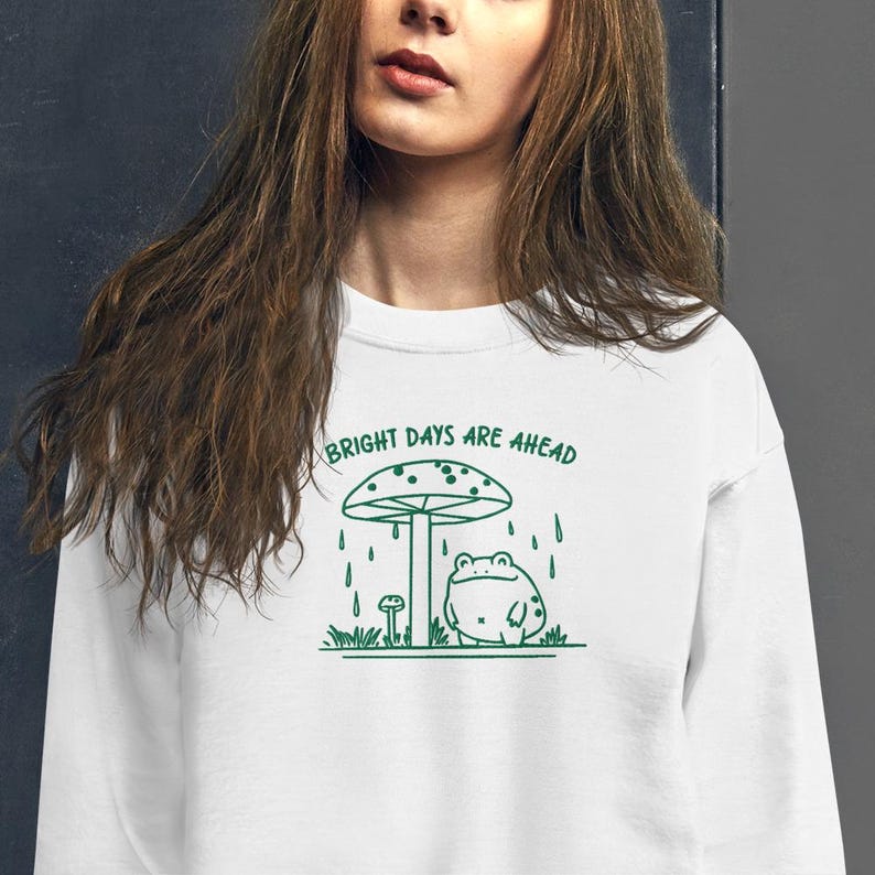 Threadmire © - Get ready to hop into cozy vibes with our Embroidered Cute Frog Under Mushroom Shirt, a whimsical nature tee that’s perfect for animal lovers and those who appreciate positive quotes! This delightful sweatshirt not only keeps you comfy