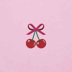 May include: Two red cherries with green stems and a pink bow tied at the top.