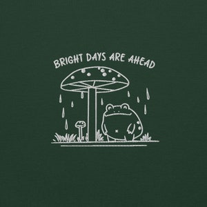 Threadmire © - Get ready to hop into cozy vibes with our Embroidered Cute Frog Under Mushroom Shirt, a whimsical nature tee that’s perfect for animal lovers and those who appreciate positive quotes! This delightful sweatshirt not only keeps you comfy