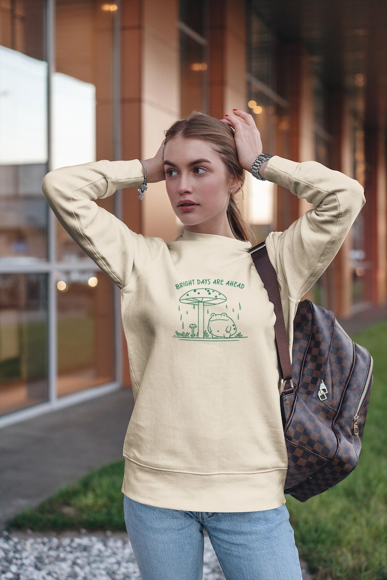 Threadmire © - Get ready to hop into cozy vibes with our Embroidered Cute Frog Under Mushroom Shirt, a whimsical nature tee that’s perfect for animal lovers and those who appreciate positive quotes! This delightful sweatshirt not only keeps you comfy