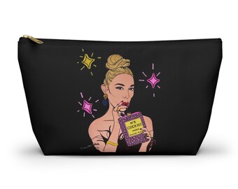 May include: Black zippered cosmetic bag featuring a pop art style illustration of a woman holding a perfume bottle. The bottle reads "N°5 Cockies Paris Eau de Plaisir". Pink and yellow starbursts are in the background.
