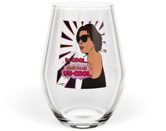 May include: A clear stemless wine glass featuring a graphic illustration of a person with dark hair wearing sunglasses. The design includes a pink speech bubble with the text "Be cool... don't be all UN-COOL." and black radiating lines.