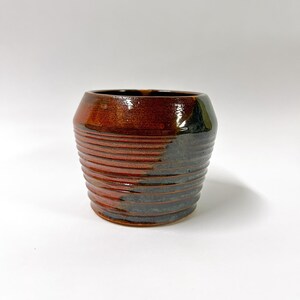 May include: A brown and black ceramic cup with a textured, ribbed design. The cup is glazed and has a glossy finish.
