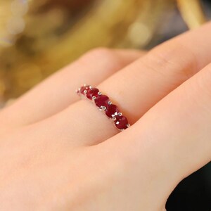 Pu&ograve; includere: Un anello color argento con una fila di cinque rubini rotondi rosso scuro, incastonati in singole griffe di metallo. Le pietre sono disposte orizzontalmente lungo la parte superiore dell'anello, mostrando un colore cremisi vibrante.