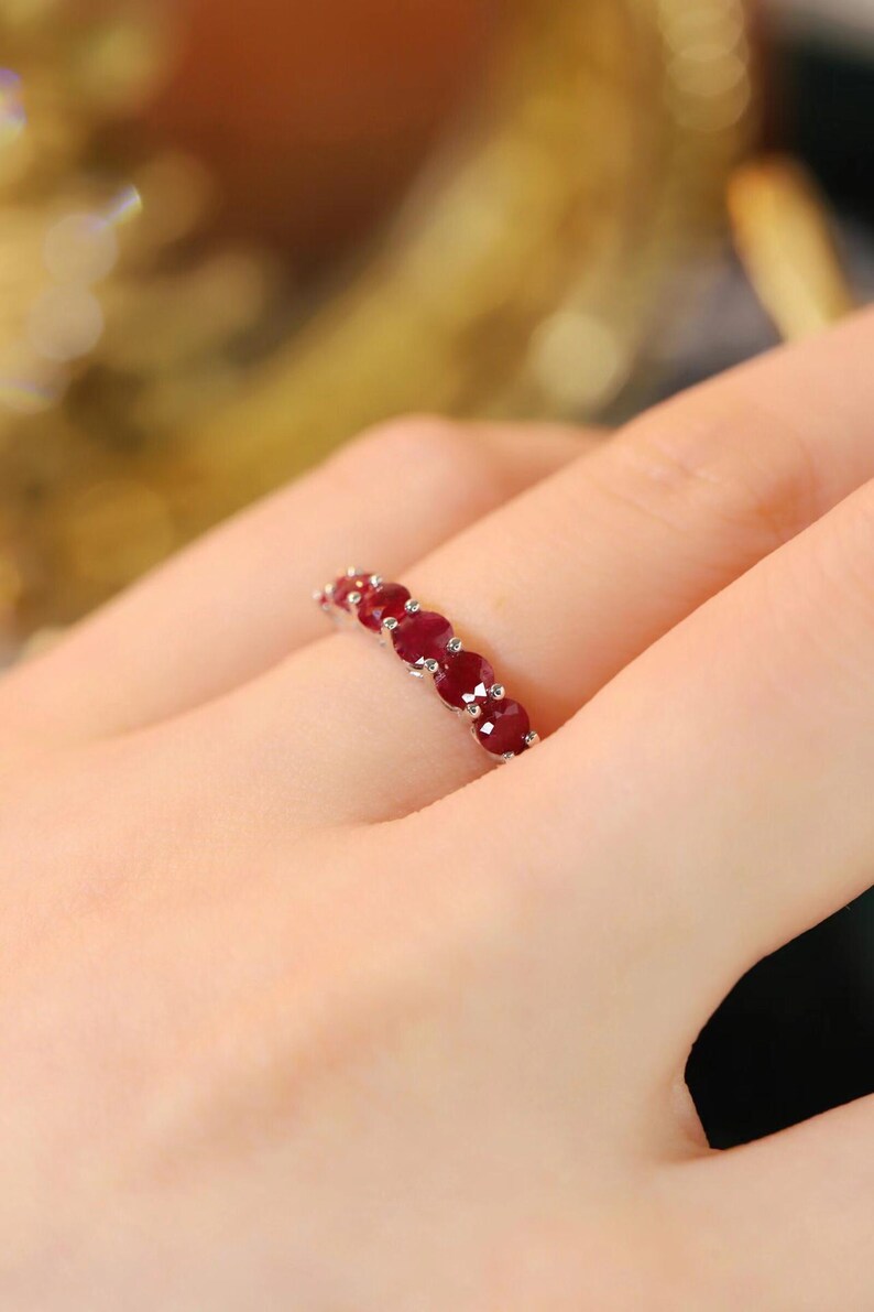 Pu&ograve; includere: Un anello color argento con una fila di cinque rubini rotondi rosso scuro, incastonati in singole griffe di metallo. Le pietre sono disposte orizzontalmente lungo la parte superiore dell'anello, mostrando un colore cremisi vibrante.
