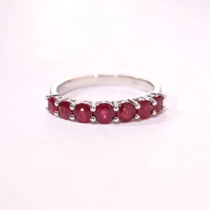 Pu&ograve; includere: Un anello color argento caratterizzato da una fila di sette rubini rosso intenso a taglio rotondo, montati su griffe. La fascia &egrave; liscia e metallica, mostrando una disposizione coerente di gemme lungo l'arco anteriore del gioiello.