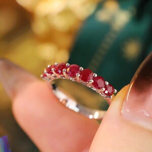 Pu&ograve; includere: Un anello color argento con una fila di sette rubini rotondi rosso scuro montati a griffe. La fascia &egrave; sottile e metallica, caratterizzata da una finitura lucida che riflette la luce sulle gemme circolari disposte in linea orizzontale.