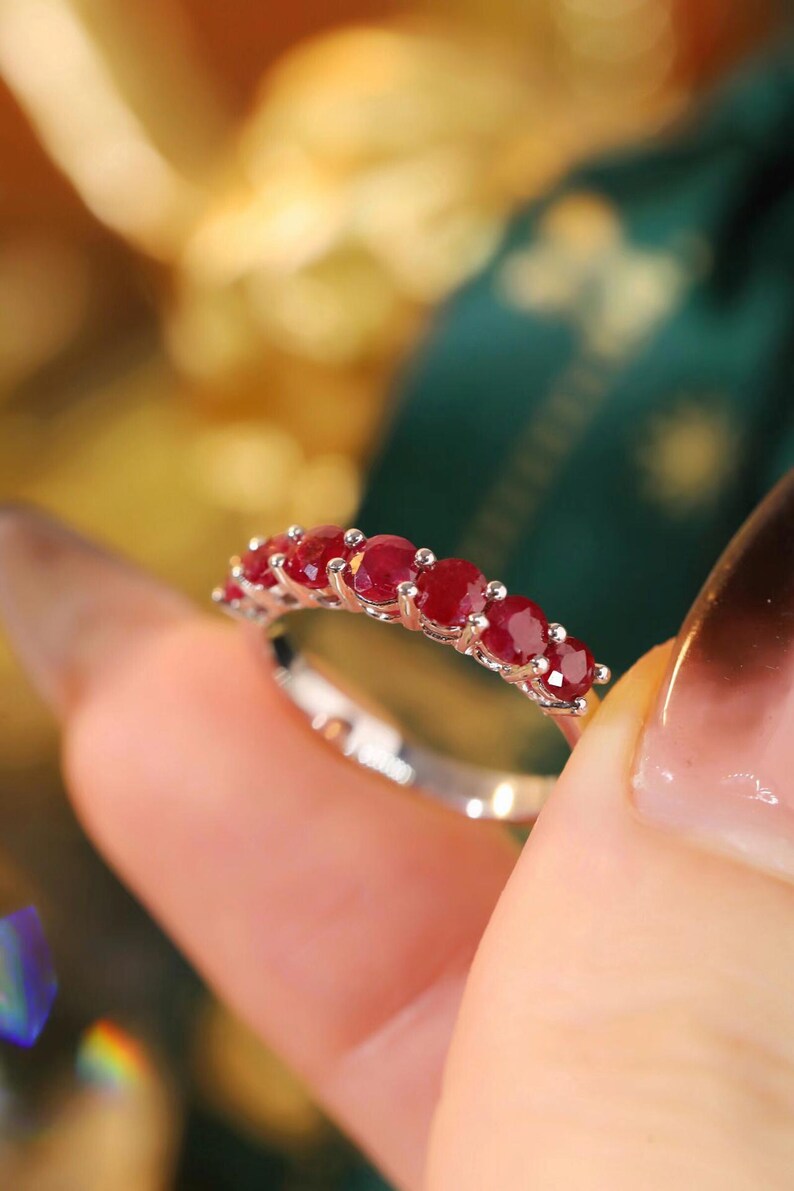 Pu&ograve; includere: Un anello color argento con una fila di sette rubini rotondi rosso scuro montati a griffe. La fascia &egrave; sottile e metallica, caratterizzata da una finitura lucida che riflette la luce sulle gemme circolari disposte in linea orizzontale.