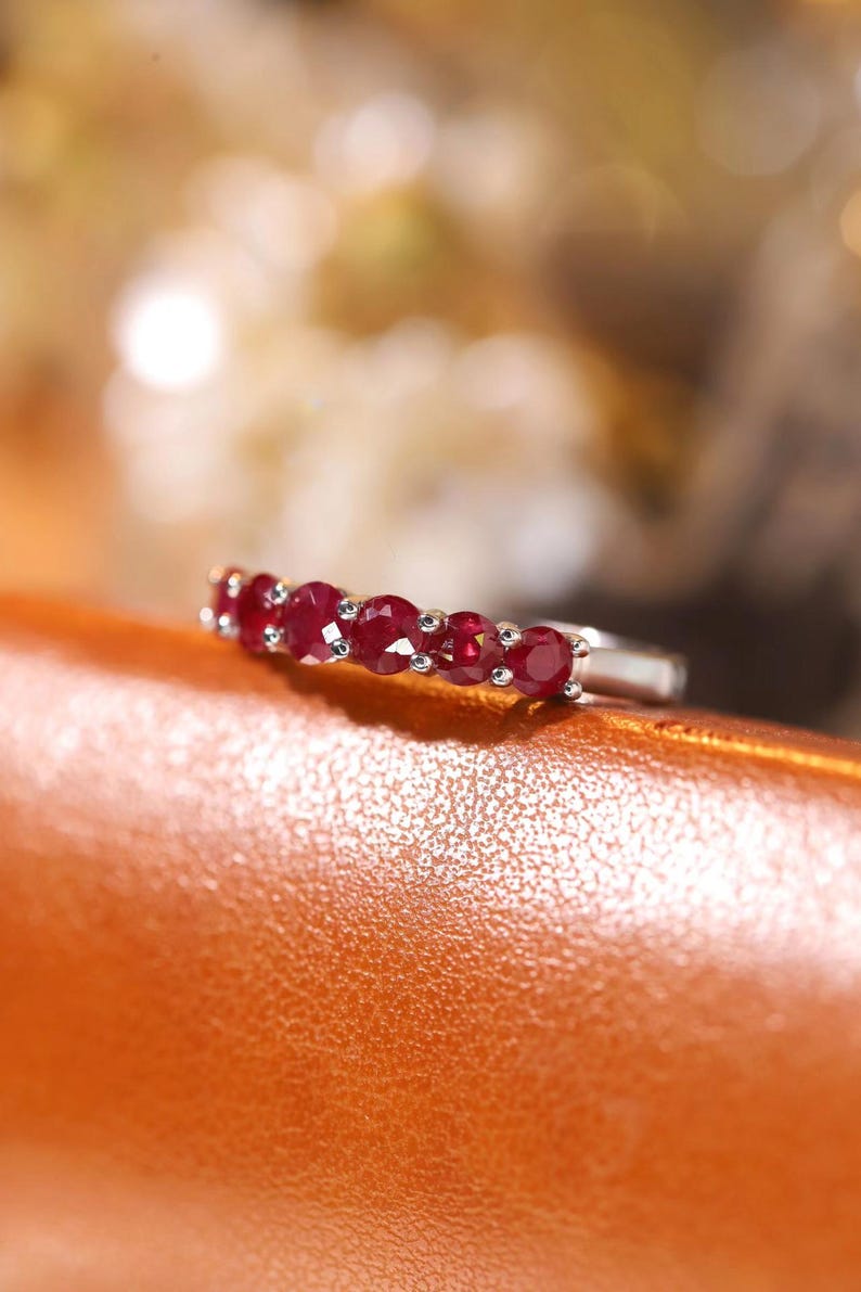 Pu&ograve; includere: Un anello in tonalit&agrave; argento con una fila di sei rubini rosso intenso a taglio rotondo, montati singolarmente su griffe. Le pietre sono disposte orizzontalmente sulla parte superiore della fascia, mostrando una superficie sfaccettata.