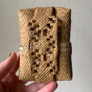 May include: A small, woven basket with a decorative pattern. The basket is made of natural materials and has a light brown colour.