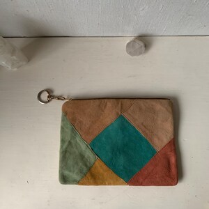 May include: A patchwork suede clutch bag with a zipper closure and a gold key ring. The bag is made of five different colored suede pieces: brown, green, teal, orange, and red.