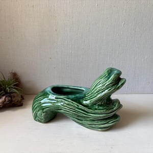 May include: A glossy, green ceramic planter shaped like a stylized tree branch. The planter has a small, open basin for holding plants or other decorative items. The surface has a textured, ridged appearance.