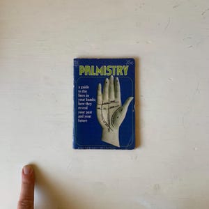 May include: A vintage paperback book titled "Palmistry" with a blue cover. The cover features a hand with lines marked, and text that reads "a guide to the lines in your hands; how they reveal your past and your future."