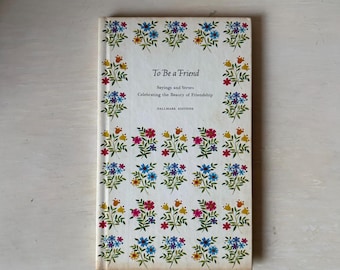 Puede incluir: Un libro de tapa dura blanco titulado To Be a Friend: Sayings and Verses Celebrating the Beauty of Friendship, Hallmark Editions. La portada presenta un patrón repetitivo de pequeñas ramas de flores coloridas en tonos azul, rojo y amarillo.