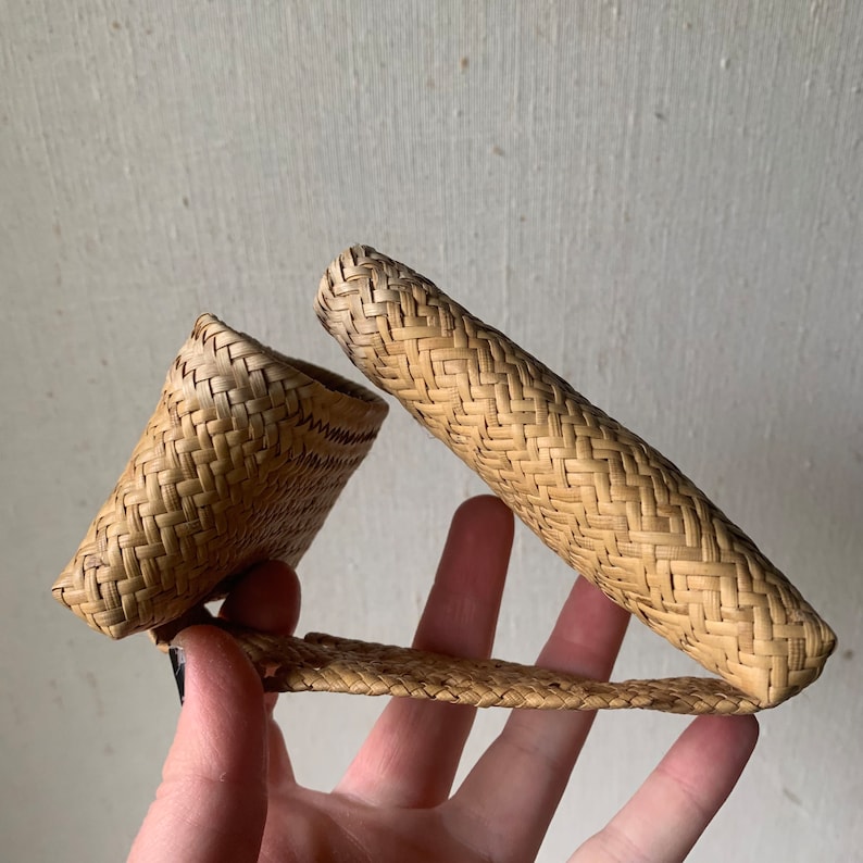 May include: A woven straw wallet in a light brown colour with a woven pattern. The wallet is folded in half and held in a hand.