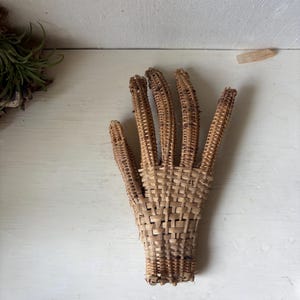 May include: A woven wicker hand sculpture in a natural light brown color. The fingers are individually crafted, and the palm is woven with a tight pattern. The sculpture is placed on a white surface.