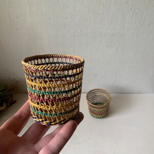 May include: Two small woven baskets with a colorful striped pattern. The baskets are made of natural materials and have a cylindrical shape.