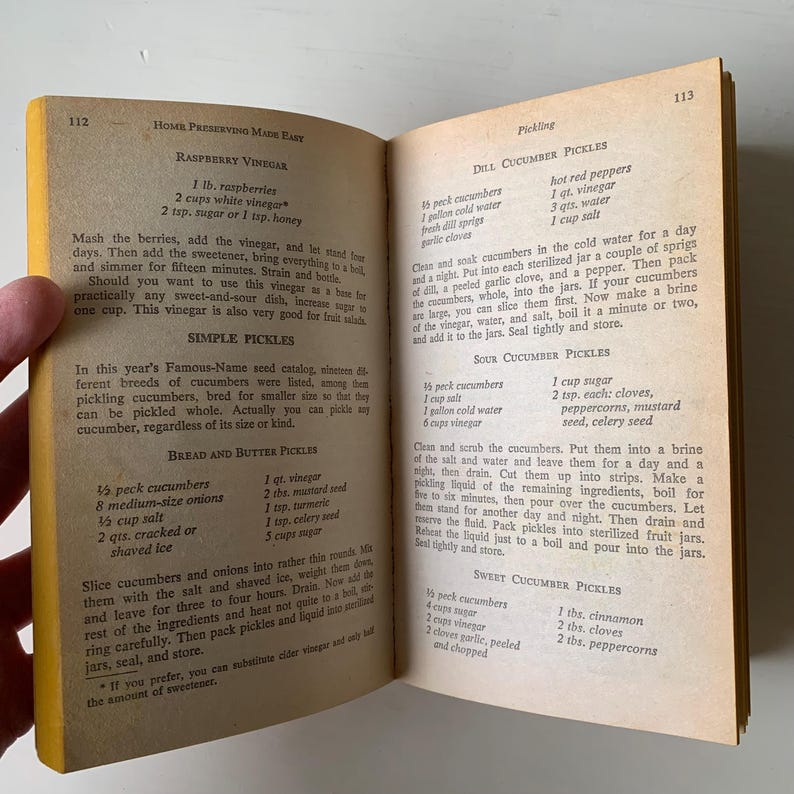 May include: A vintage cookbook page with recipes for raspberry vinegar, simple pickles, bread and butter pickles, dill cucumber pickles, sour cucumber pickles, and sweet cucumber pickles. The recipes include ingredients and instructions for making each type of pickle.