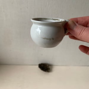 May include: White ceramic mug with a rounded body and a small handle. The mug has the word "enough" written on the side in gold lettering.