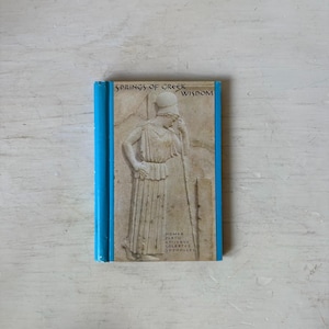May include: A hardcover book titled "Springs of Greek Wisdom" with a blue spine. The cover features a relief sculpture of a classical figure. The names Homer, Plato, and others are listed.