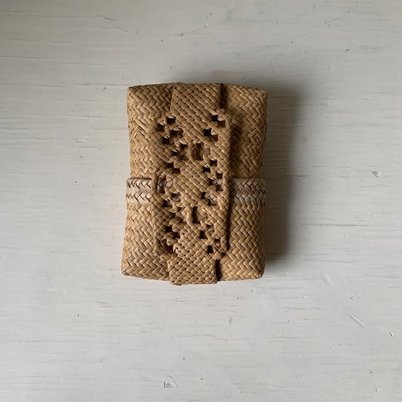 May include: A small, rectangular, woven basket with a light brown colour and a pattern of small holes. The basket is made of natural materials and has a simple, elegant design.