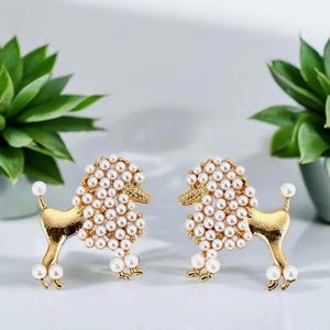 May include: A pair of gold-tone earrings shaped like poodles, each covered in white faux pearls.