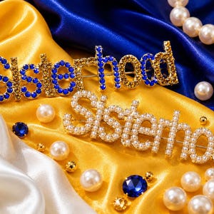 May include: Two metal brooches featuring the word Sisterhood in script lettering. One brooch is encrusted with blue and gold-toned crystals, while the other is decorated with white faux pearls. Both pieces are displayed alongside loose pearls and crystals.