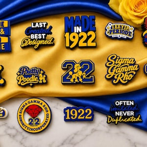 Könnte beinhalten: Eine Sammlung von blau-goldenen Schuhanhängern mit verschiedenen Motiven, darunter die Texte IT'S THE BLUE & GOLD FOR ME, LAST GREATED BEST DESIGNED, MADE IN 1922, IEEYIP PERIODT, ein Pudel, die Zahl 22, Sigma Gamma Rho und ein rotes Diamantlogo.