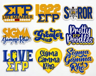 May include: A collection of nine embroidered patches featuring blue and gold designs with text including Sigma Gamma Rho, 1922, Life Member, Soror, Pretty Poodles, Greater, and Love. The patches display various fonts, shapes, and symbols.