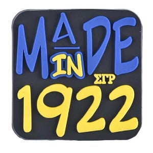 Könnte beinhalten: Ein schwarzes Quadrat mit abgerundeten Ecken mit den Worten "MADE IN 1922" in Blau und Gelb. Der Text ist mit einer fetten Schriftart gestaltet. Die Buchstaben "MADE" sind blau, "IN" ist gelb und "1922" ist gelb.