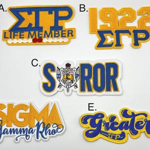 Könnte beinhalten: Gestickte Aufnäher in Gold, Blau und Weiß. Die Aufnäher zeigen griechische Buchstaben und Sätze wie "Life Member", "1922", "Soror", "Sigma Gamma Rho" und "Greater". Diese Aufnäher sind wahrscheinlich für eine Studentenverbindung.