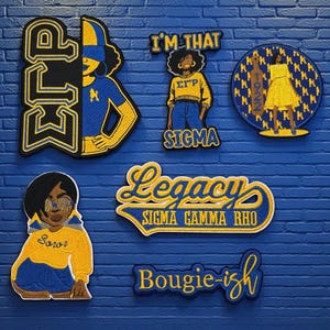 May include: A selection of embroidered patches in blue, yellow, and black. The designs feature sorority symbols, figures, and text including "ELP", "I'M THAT SIGMA", "Legacy SIGMA GAMMA RHO", and "Bougie-ish". The patches are shown against a blue brick wall.