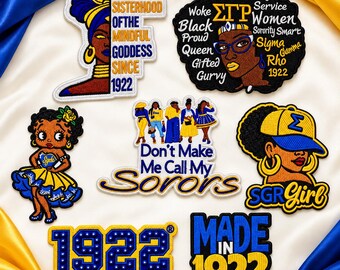 May include: A collection of seven embroidered patches featuring blue and gold themes. Designs include a woman in a headwrap, a word cloud with Sigma Gamma Rho symbols, a cartoon character, a group of women, a woman in a cap, and the year 1922.