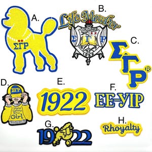 Puede incluir: Un conjunto de ocho parches bordados con las letras griegas "ΣΓΡ" en azul y amarillo. Los parches incluyen un caniche, un escudo, una niña con un sombrero y el año "1922".