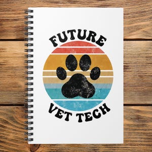 May include: A white spiral-bound notebook featuring a circular graphic with horizontal stripes in red, orange, yellow, and blue. A black paw print is centered in the circle, with the black text FUTURE VET TECH arched above and below the graphic.