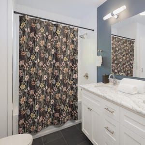May include: A floral shower curtain with a dark background and a pattern of various flowers in shades of pink, yellow, and green. The curtain hangs in a bathroom with white walls and a white vanity.