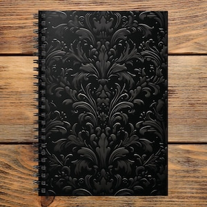 May include: A black spiral-bound notebook featuring a raised, glossy damask pattern across the front cover. The notebook has a rectangular shape with a black metal coil binding along the left side, contrasting with the matte black background.