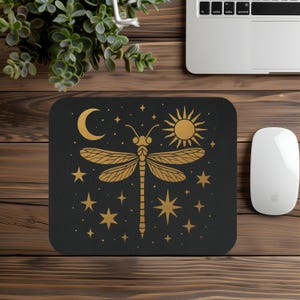 May include: Black mousepad with a gold dragonfly design, a crescent moon, sun, and stars. The mousepad is rectangular with rounded corners. The design is a celestial theme.