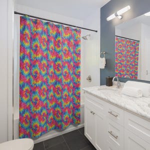 May include: A shower curtain featuring a vibrant tie-dye pattern with swirling colors of hot pink, bright yellow, and electric blue. The fabric hangs from a black rod with metal rings, covering the bathtub area in a bathroom setting.