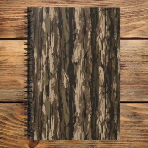 May include: A spiral-bound notebook featuring a vertical tree bark camouflage pattern in shades of dark brown, olive green, and tan. The notebook has a black metal wire coil binding along the left side and a rectangular shape with rounded corners.