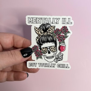 May include: White sticker with a black and white illustration of a skull wearing leopard print sunglasses and a bun with a red rose behind it. The skull is holding a glass of red wine. The text "Mentally Ill But Totally Chill" is printed on the sticker.